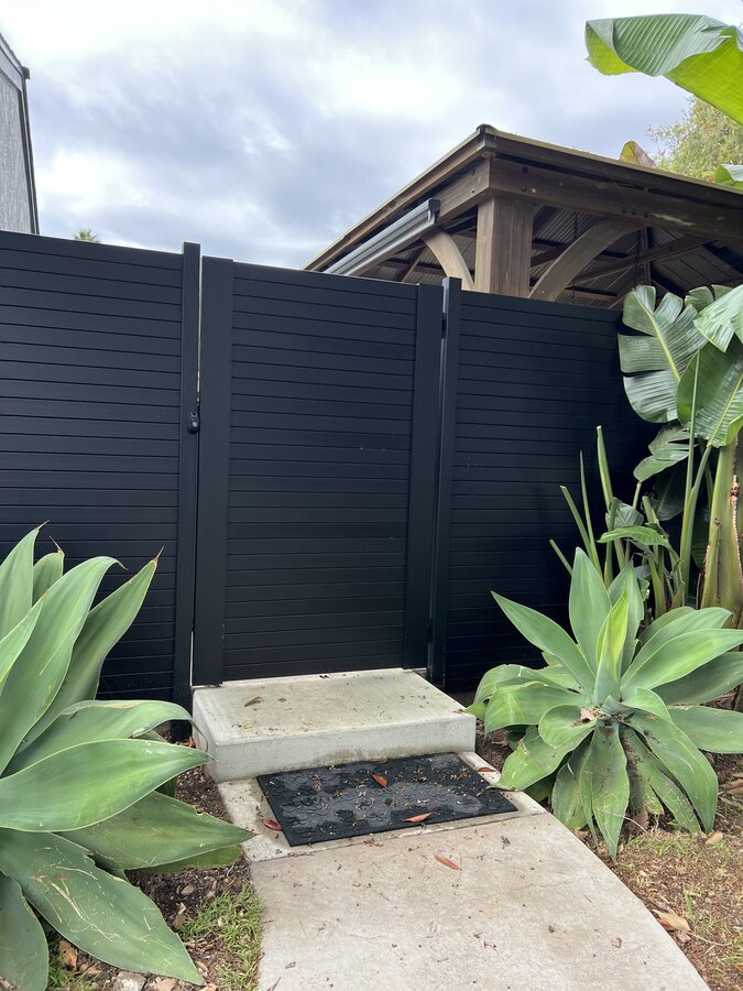 Black horizontal aluminum fence and matching gate among tropical landscaping in Goleta