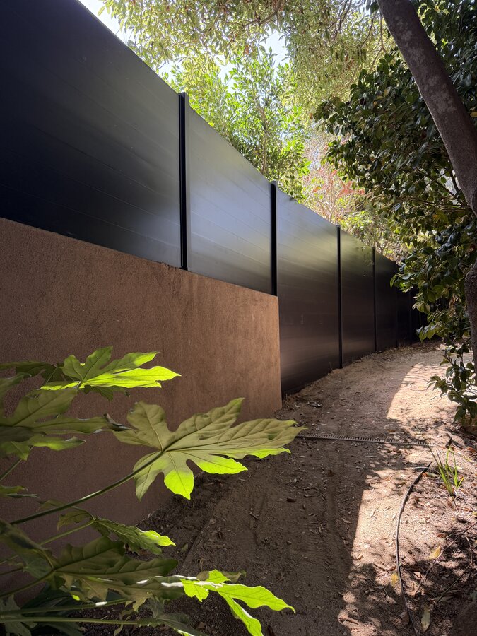 Black horizontal aluminum fence atop a stucco retaining wall in Montecito