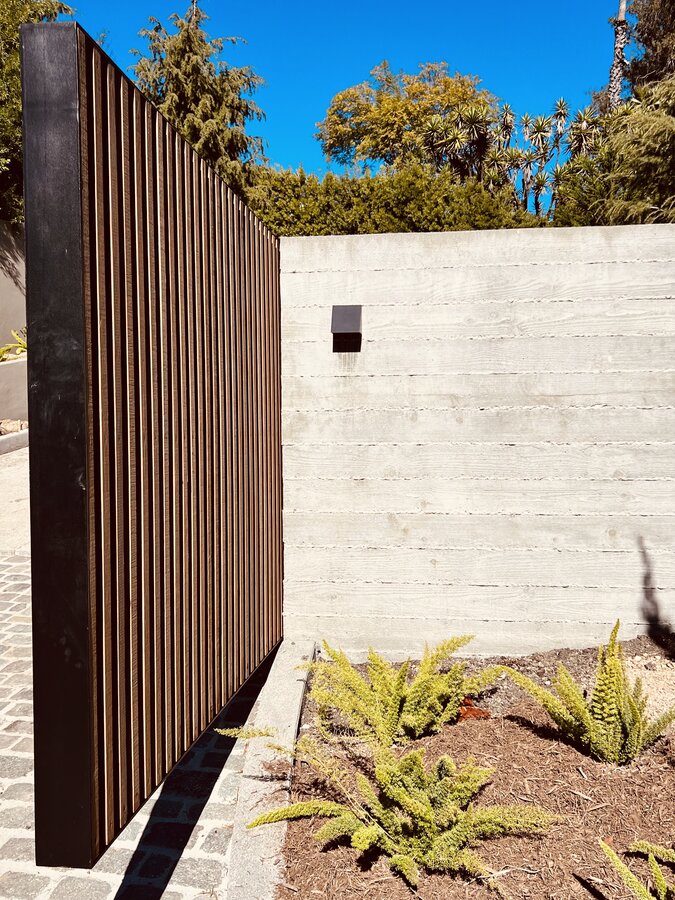 Black vertical slat gate against a poured concrete wall in Montecito