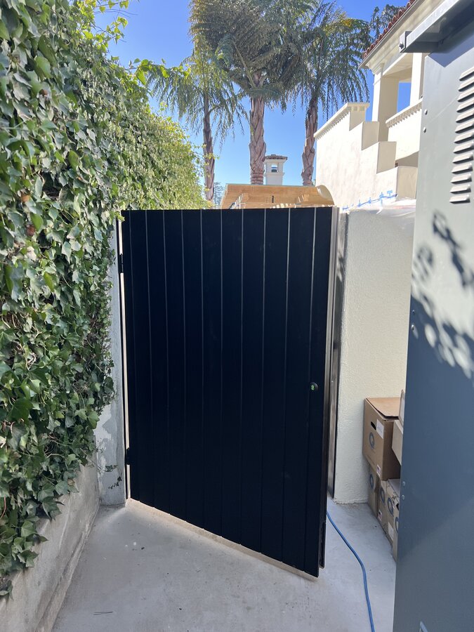 Black vertical slat gate in a narrow ivy-lined alcove in Montecito