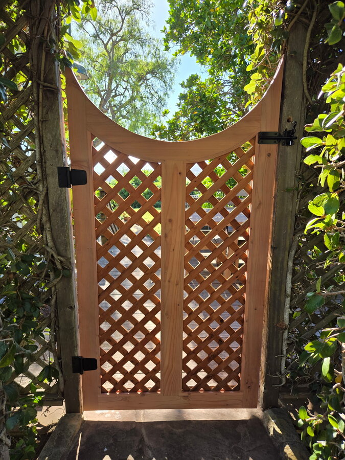 Curved lattice-top cedar gate through a hedge archway in Montecito