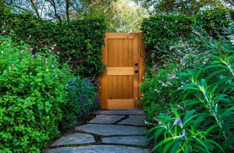 Custom wood door gate set into a flowering hedge