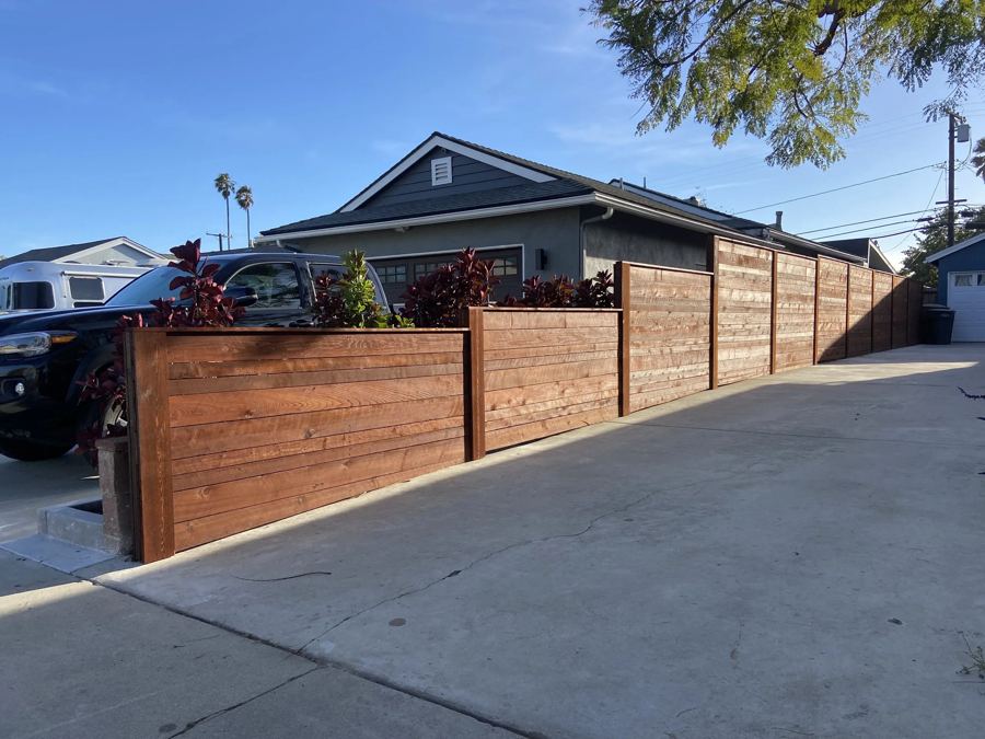 Horizontal redwood fence with built-in planters along a driveway