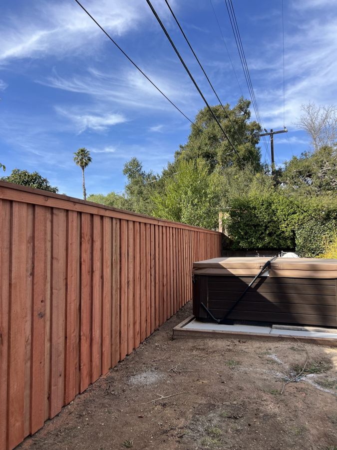 Stained redwood board fence beside a spa