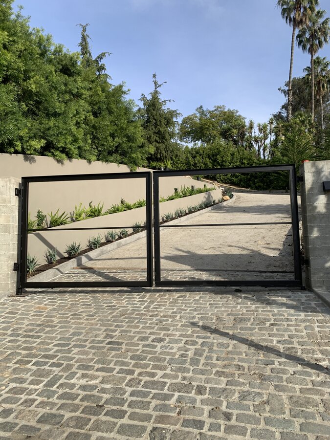 Steel-framed double swing driveway gate over cobblestone with succulent beds in Hope Ranch