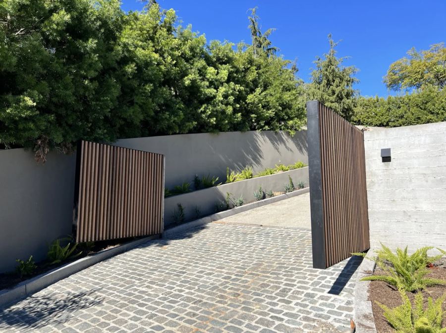 Steel-framed vertical slat driveway gates open over a cobblestone drive