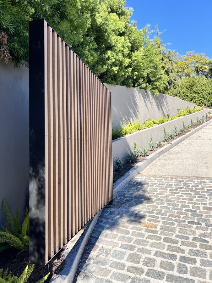 Vertical hardwood and steel slat gate along a cobblestone driveway in Montecito